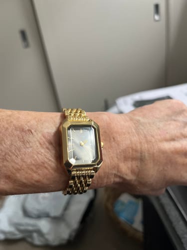 Customer wearing the gold CLAIRE DE MAINS watch with a rectangular face on their wrist.