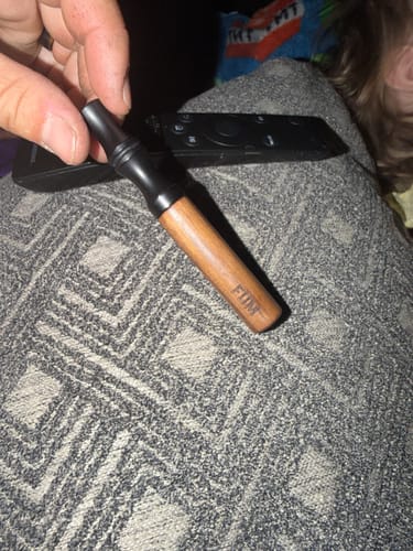 Customer's hand holding the wooden FÜM device with its black mouthpiece, resting on a gray textured surface.