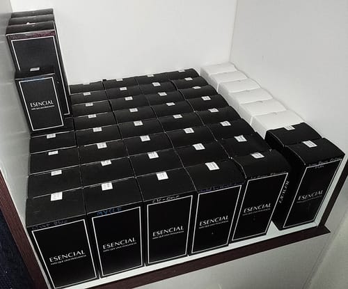 Foto de un cliente mostrando numerosas cajas del perfume ESENCIAL apiladas en un estante.