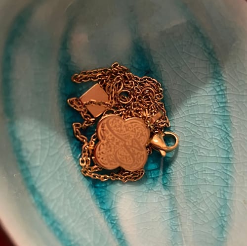 Customer's gold Love Necklace with an engraved clover-shaped pendant resting in a turquoise bowl.