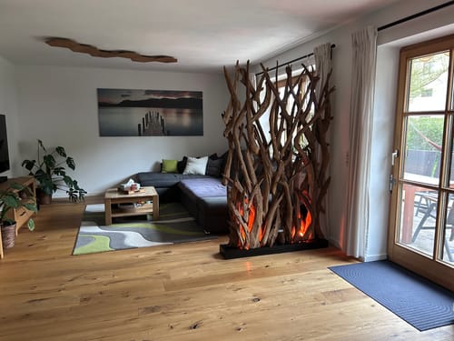 Kundenfoto des Design Raumteilers BLUMA, der in einem Wohnzimmer mit warmer Sockelbeleuchtung auf einem Holzboden steht.