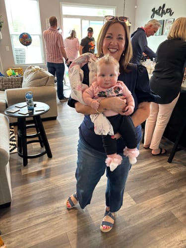 Reviewer smiling while holding a baby, wearing the navy Puffed Blouse Sleeve Solid Body Tee with jeans indoors.