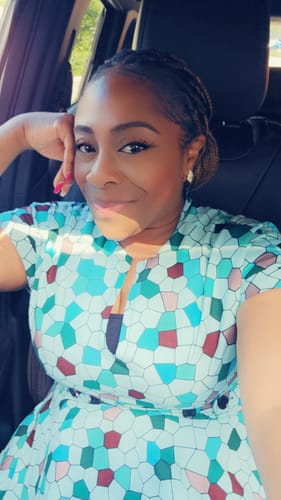 A reviewer wearing the GINA AFRICAN PRINT MIDI DRESS in a car, showing its colorful geometric pattern and front zip detail.