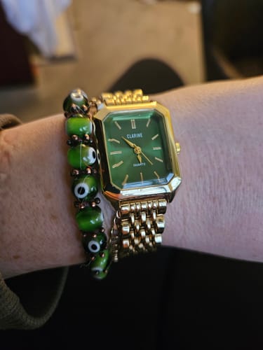 A reviewer's wrist wearing the CLAIRE DE MAINS watch with a green rectangular face and a gold-colored band.