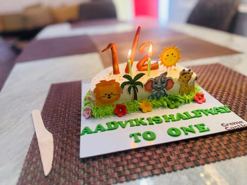Customer's Jungle Semi Cake decorated for a half birthday with cute animal figures and two lit candles on a table.