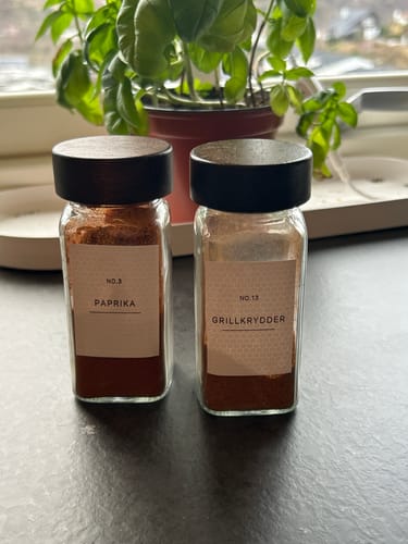 Anmelderens krydderetiketter for Paprika og Grillkrydder på to pene krydderglass på en kjøkkenbenk.