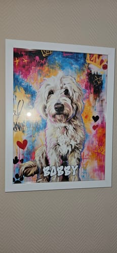 Kunde zeigt einen weißen Posterrahmen mit einem farbenfrohen Porträt eines Hundes namens 'Bobby', der an der Wand hängt.