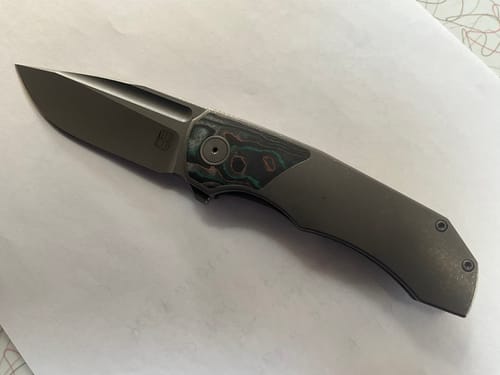 Reviewer's BergBlades Tick knife showing its dark stonewash finish and unique CamoCarbon handle inlay.