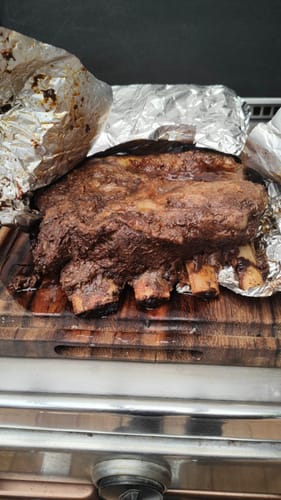 Prime Rib de un cliente, cocido y jugoso, sobre una tabla de cortar con papel aluminio.