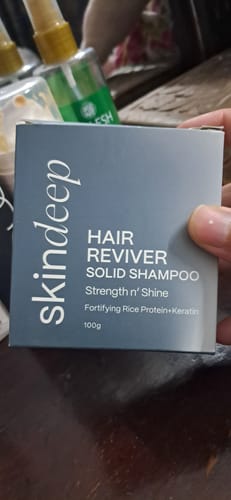 Customer holding the grey box for the HAIR REVIVER Solid Shampoo against a blurred background.