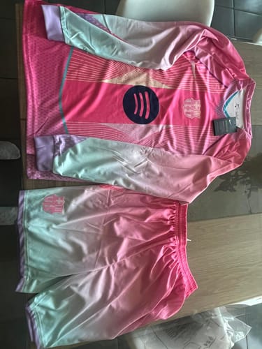 Client montrant le maillot rose à manches longues et le short assorti, posés à plat sur une table.