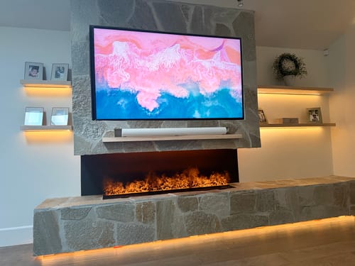 Customer's Aquafire fireplace installed in a large stone hearth, displaying vibrant, realistic flames.