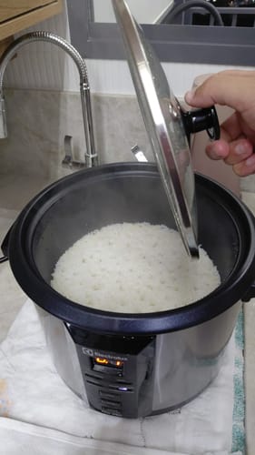 Cliente mostrando o arroz da Cesta Básica Mognoproduct pronto em uma panela elétrica.