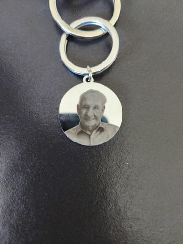 Kunde zeigt den runden Schlüsselanhänger mit einem eingravierten Porträtfoto auf einer dunklen Oberfläche.