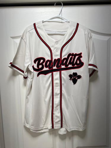 Customer's custom cream baseball jersey for the 'Bandits' team hanging on display.