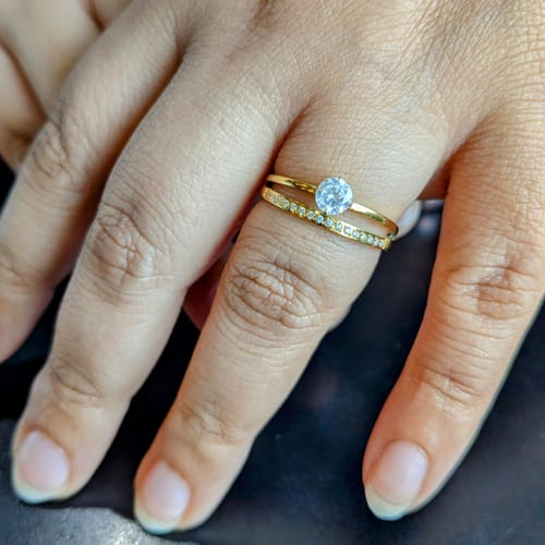 Customer's hand showing the stacked gold-colored Princess Ring with its round solitaire and delicate pavé band.