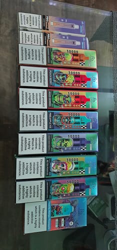 Ein Rezensent zeigt eine Reihe von bunten RANDM TORNADO 30000 Verpackungen, die auf einem Glastisch liegen.