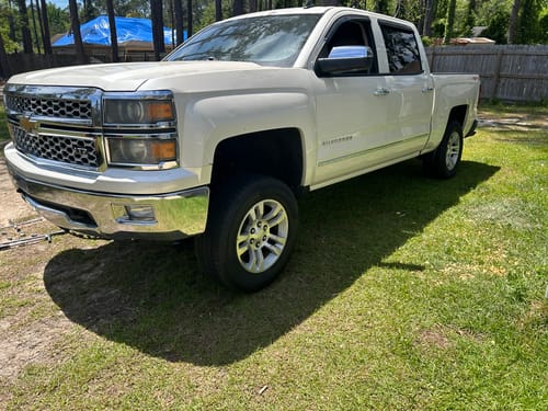 Customer's lifted white Chevy Silverado truck after installing the upper control arms, parked on a grassy lawn.