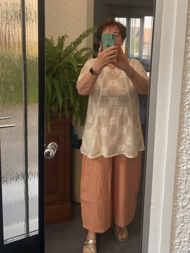 Une cliente porte la Tunique Elise en coton crocheté ivoire avec un pantalon large couleur saumon.