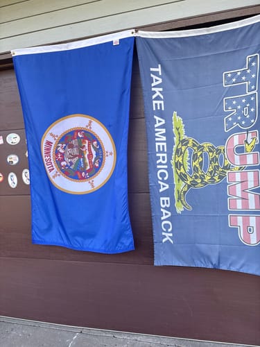 Customer's old style State of Minnesota Flag hanging on a wall next to another flag.