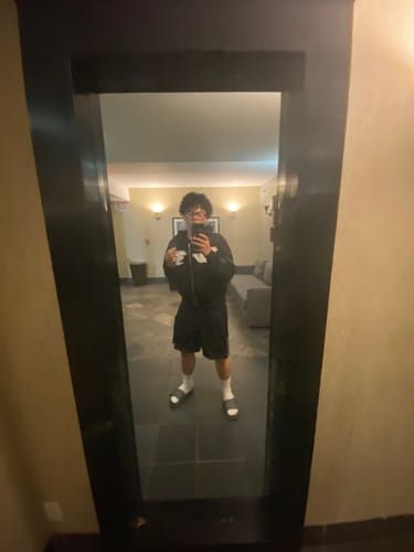 Reviewer takes a full-length mirror selfie wearing the black Embroidery Logo Hoodie with shorts and slides.