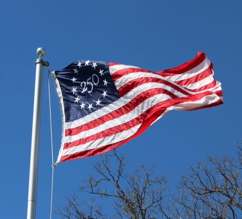 Customer's America 250 Collector's Edition Betsy Ross Flag waving on a flagpole against a clear blue sky.