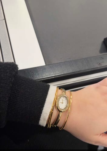 Reviewer's wrist wearing the elegant Diana Gold White watch, styled with other gold bracelets.