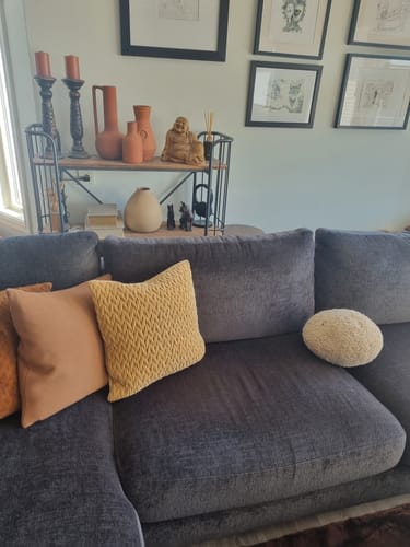 Kundens flettede putetrekk i jordfarge vist på en mørk sofa sammen med andre puter.