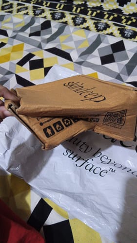 Customer holding the damaged cardboard box their Peptide Lip Glaze arrived in, showing a bent corner.