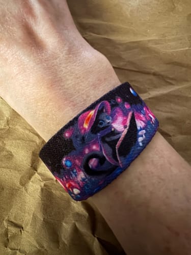 A reviewer wears the Purrfectly Powerful Bracelet on their wrist, showing the vibrant, magical cat design.