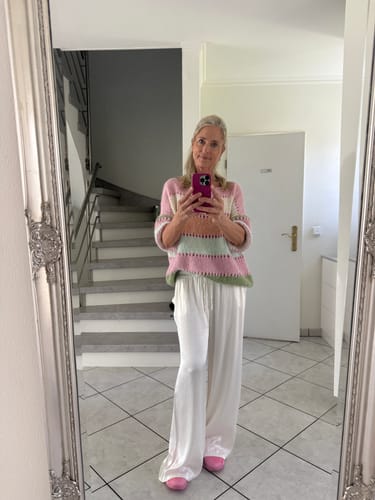 Kundin trägt den Pastell Stripe Pullover mit einer weiten, weißen Satinhose bei einem Spiegel-Selfie.