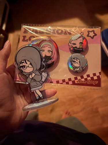 Customer holding a cute Alien Stage Badge Set with a character standee and two shiny, holographic badges in the packaging.