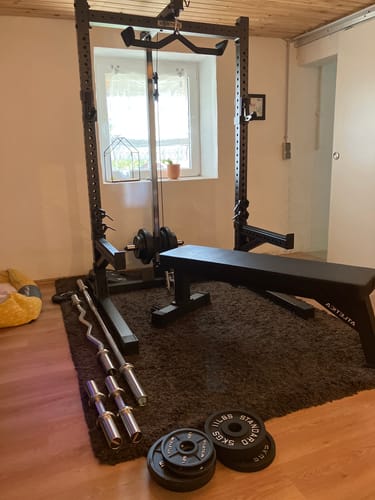 Ein Kunde zeigt sein R7 Rider Squat Rack in einem Heimstudio, mit Hantelbank und Gewichten davor.