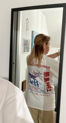 Reviewer in a mirror showing the back graphic of the white Torii Gate T-Shirt, which has a regular fit.