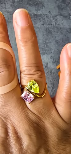 Customer's hand wearing the gold Navae Birthstone Ring with a light green pear-cut stone and a pink radiant-cut stone.