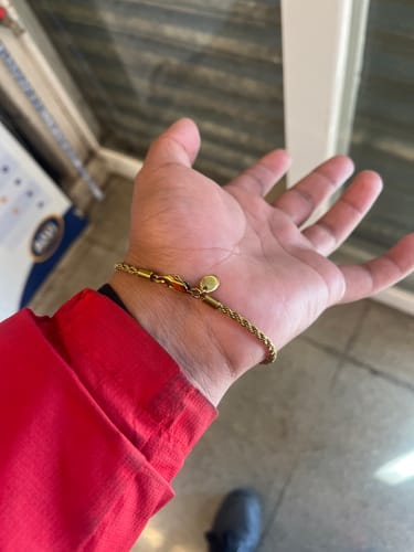 Un cliente muestra la Pulsera Rope Oro 3mm en su muñeca, junto a la manga de una chaqueta roja.
