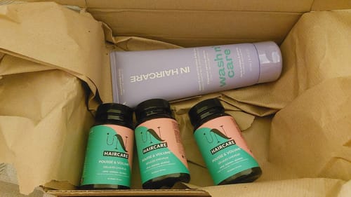 Un client montre trois flacons de Gélules - Cure pousse de cheveux dans la boîte de livraison.