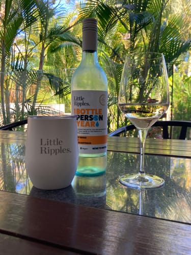 Reviewer's white Travel Wine Tumbler on an outdoor table next to a bottle and glass of white wine.