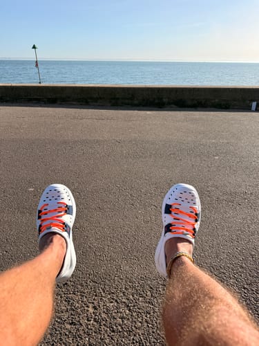 Customer's first-person view of their white Early Bird Wildpools with orange laces by the sea.