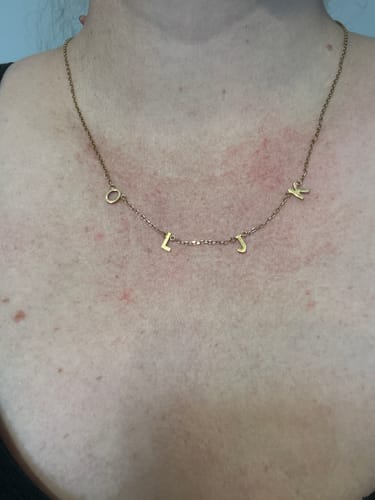 Customer wearing a gold-colored necklace with initials around their neck.