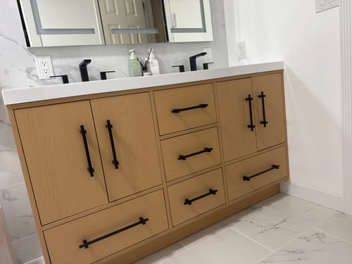 Reviewer's installed Belgian Modern Vanity II with a light wood finish and contrasting black hardware in a modern bathroom.