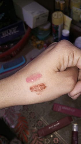 Reviewer's hand showing two glossy swatches of Peptide Lip Glaze in a soft pink and a brown terracotta shade.