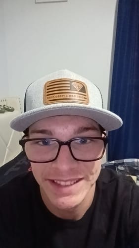 Customer smiling while wearing the grey Salute Trucker Hat, showing its front leather patch.