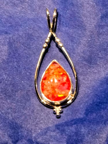 Reviewer's Double Spade Memorial Pendant with a sparkly orange opal, shown on a blue cloth background.