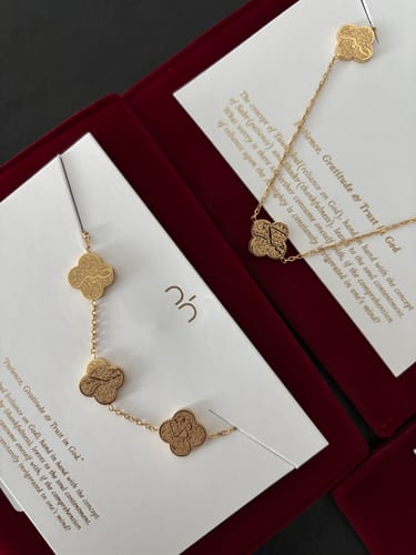 Reviewer's two gold Hardship & Ease Necklaces displayed in their red presentation boxes.