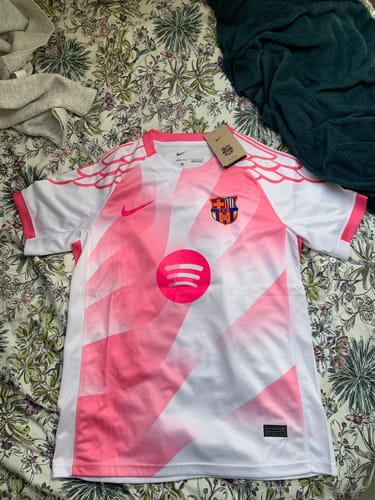 Photo d'un client montrant le maillot de Barcelone rose et blanc, posé à plat sur une surface.