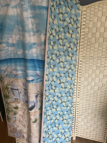 Customer's blue floral cotton fabric hanging next to a seaside shower curtain and a wicker room divider.