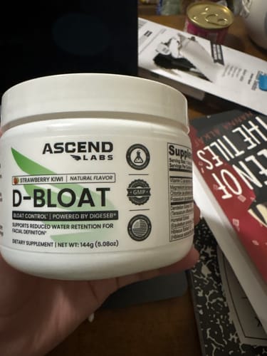 Customer holding a white tub of D-BLOAT dietary supplement, showing the Strawberry Kiwi flavor.