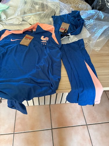 Client montrant l'ensemble France bleu 25/26, haut et pantalon, posés sur une table après déballage.