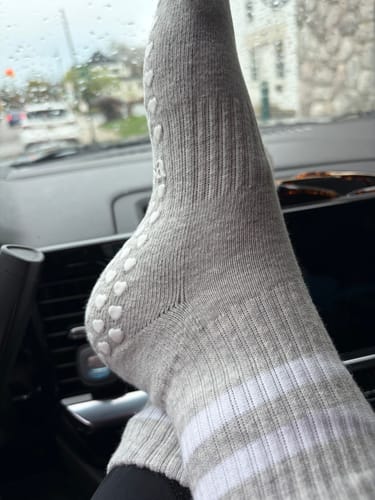 Customer wearing the gray grip socks in a car, showing the white stripes and heart-shaped grips on the heel.